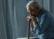 Senior sad man leans on a cane while sitting on sofa Senior sad man leans on a cane while sitting on sofa